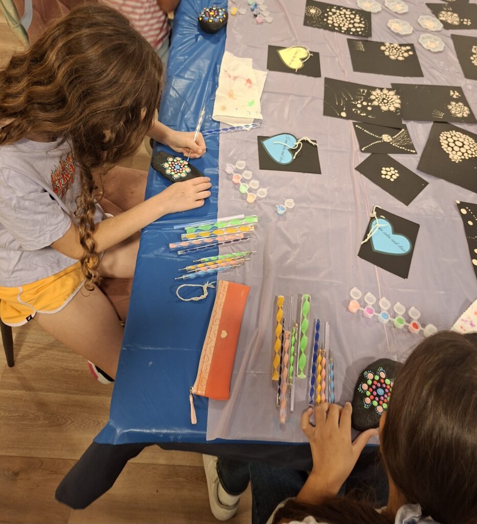 Child carefully painting a mandala pattern on a stone, learning dot art techniques during the workshop.