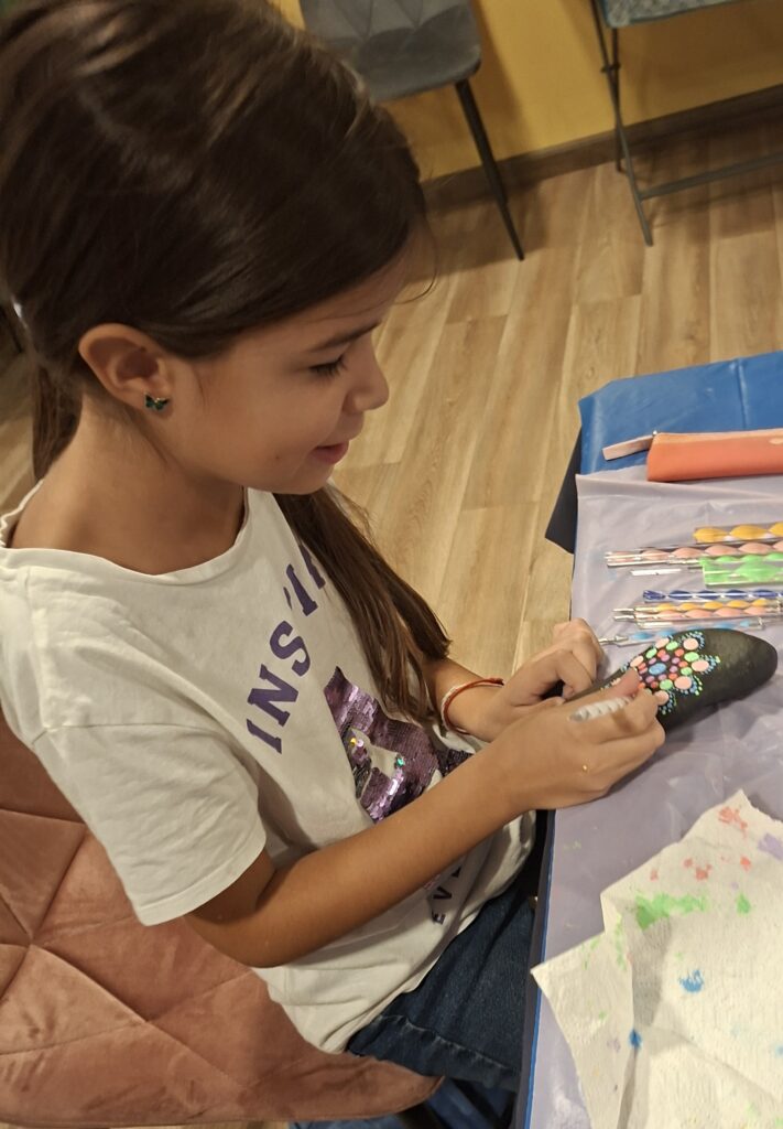 Young participant creating a colorful mandala design on a black stone at the Mandala Dot Art Kids Workshop.